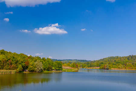 Beautiful scene of colorful forest on hilly landscape over lake.