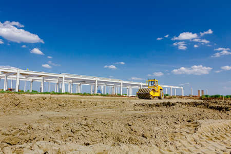 Huge road roller with spikes is compacting soil, sand at building site.