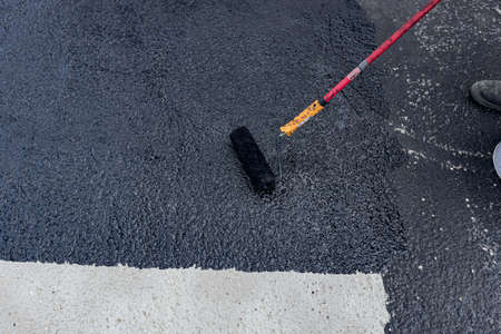 Worker is coating tarmac using a brush roller, apply the first basic protective layer of...