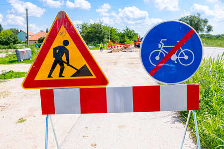 Two signs are set on the road at construction site, triangle sign, work in progress, with red and white stripes and prohibited cycling.の写真素材
