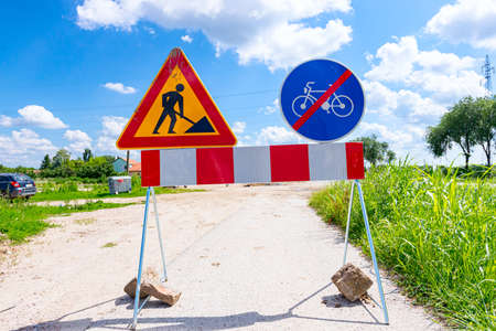 Two signs are set on the road at construction site, triangle sign, work in progress, with red and...