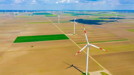 Above view on farm of large wind power turbines are standing among agricultural fields, generating...