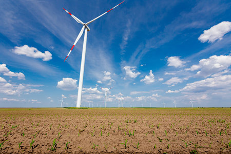 Farm of few large wind power turbines are standing among agricultural fields, generating clean...