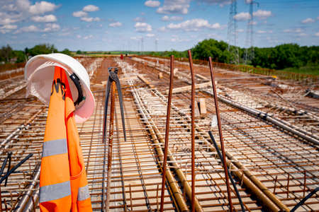 White safety helmet and metal pliers for binding wire reinforcement hung on a plastic tube, square...