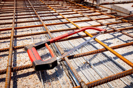 A hand hacksaw for metal set on rusty square reinforcing mesh that was placed for the strength of...