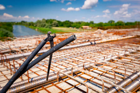 Metal pliers for binding wire reinforcement hung on a plastic tube, square rusty armature, placed...