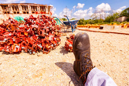 View of a worker's safety shoe on a construction site, a pile of disassembled scaffolding parts in...