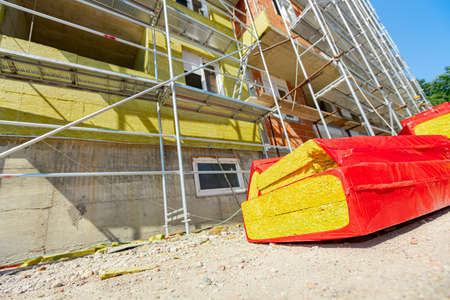 Packaging of thermal insulation material, stone wool wrapped in foil is waiting to be installed on the walls of the residential building under construction with scaffold.の写真素材