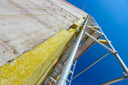 View from below on installed thermal isolation stone wool on the unfinished brick wall of residential building. The metal scaffold is placed against unfinished edifice under construction.の写真素材