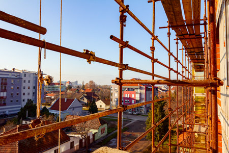 Rusty scaffold placed against unfinished edifice, new residential building under construction,...