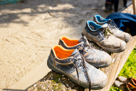 Old worn out safety shoes lined, placed on small wall near construction site as workers are pouring...