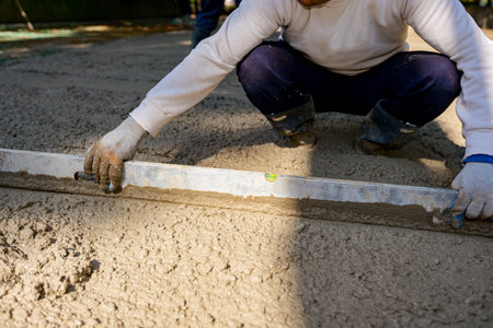 Construction worker is wearing gloves as leveling fresh concrete with metal lath after pouring.