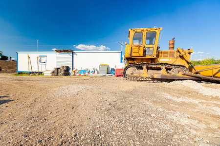 Industrial yellow earthmover parked at the construction site in front of mobile container office for...