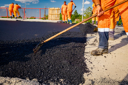 Few workers are using shovels to level, set up layer of fresh tarmac to right measures, pouring hot asphalt.の写真素材