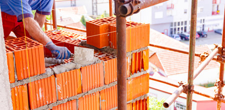 Worker is using spatula, trowel, to apply mortar on red blocks to make wall, bricklayer. Building is under construction.の写真素材
