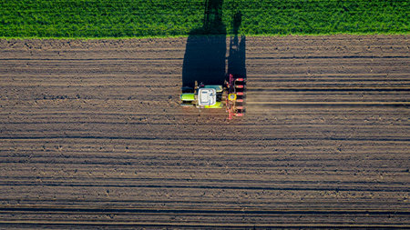 Above top view, of tractor as pulling mechanical seeder machine over arable field, soil, planting...