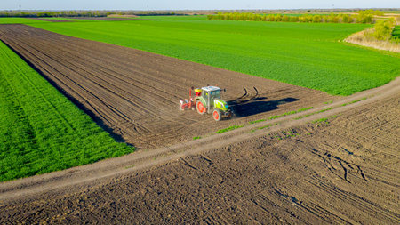 Above view, of tractor as pulling mechanical seeder machine over arable field, soil, planting new...