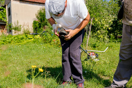Repairman with bandaged hurt hand repairs trimmer, adjusts string of trimmer head coil for mowing...