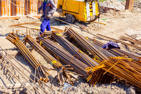 Worker takes bar from pile of selected tied bundles of reinforcement. Installed metal piles along...