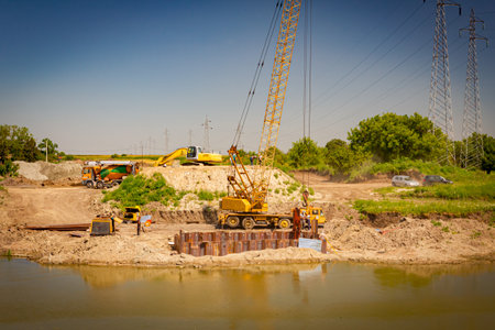 Across the water is yellow obsolete mobile crane with pneumatic hammer. Installed metal piles along...
