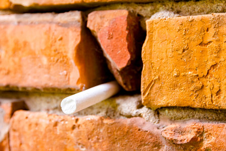 White school chalk stuck in an obsolete dilapidated wall of damaged red bricks.の写真素材
