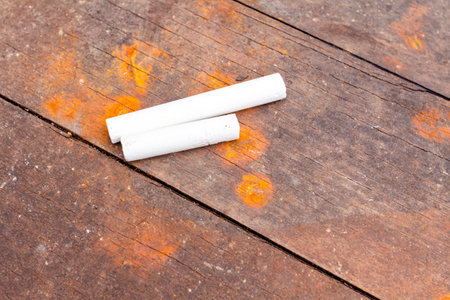 Two white school chalks placed on obsolete brown and rusty wooden planks of table.
