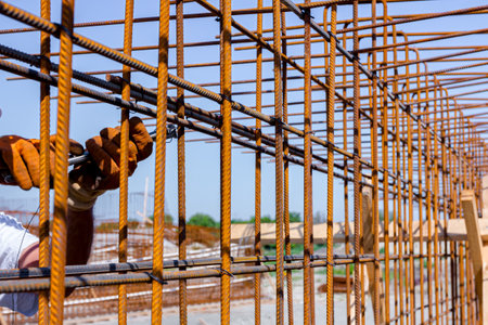 Worker is tying rebar with wire using pliers, to make a reinforcing frame for concrete beam. Works on construction siteの写真素材