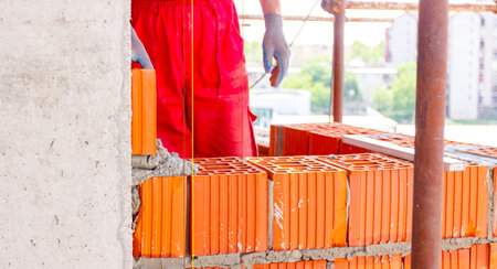 Mason, bricklayer worker is using red blocks to mount a wall next the string line to be straight.の写真素材