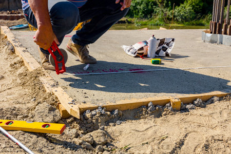 Worker in crouching position uses a land measuring tape to precise measure distance on concrete slab of bridge under construction.の写真素材