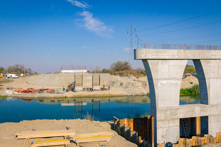 Large modern gray concrete pillar in foundation surrounded by metal piles. Planks, beams placed on...