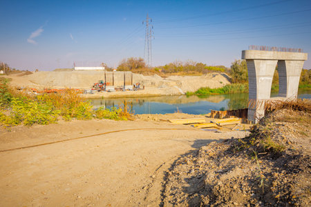 Heap of dirt, large modern gray concrete pillar in foundation surrounded by metal piles. Beams on...