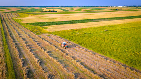 Tractor with attached mechanical rake is turning and gathering dry moved grass to arrange in long...