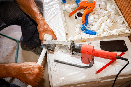 Plumber's hands as using handy power tool, iron for soldering, welding polypropylene pipes, connecting them in pipeline, workshop at indoor construction site, residential building.の写真素材