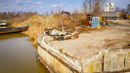 Pier, dock of concrete at river coast with piled trash of old large vessel, barge, dismantling ship in pieces, cut out rusty metal for scarp, using acetylene torch, recycling, equipment, gas tank.の写真素材