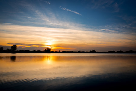 Scenic view of beautiful sunset in the evening time over lake, silhouette across water and reflection of clouds on calm water.の写真素材
