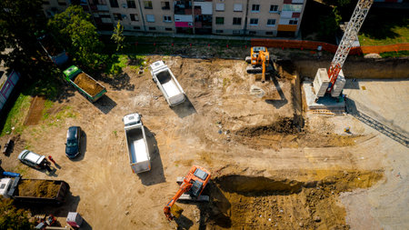 Above view on two big excavators as they digging, excavating foundation for new residential building and filling few dumper trucks with soil, ground at construction site, project in progress.の写真素材