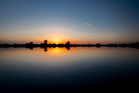 Scenic view of beautiful sunset in the evening time over lake, silhouette across water and reflection of clouds on calm water.の写真素材
