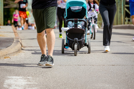 Mother pushing a stroller with a baby, child and running in a street marathon competition, at urban...