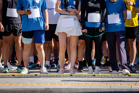 Large group of runners, athletes at start line few seconds before start their run, in a street marathon competition, crowd of people waiting for race to begin, legs and feet of runners.の写真素材