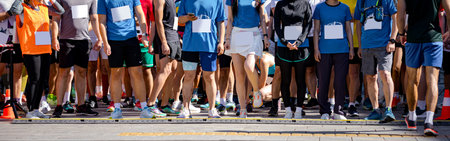 Large group of runners, athletes at start line few seconds before start their run, in a street marathon competition, crowd of people waiting for race to begin, legs and feet of runners.の写真素材