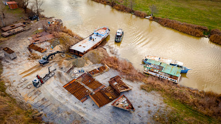 Above view over excavator, tow truck and tugboat as they pull out part of old freight vessel, barge,...