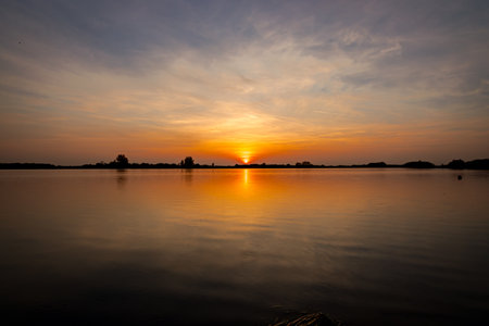 Scenic view of beautiful sunset in the evening time over lake, silhouette across water and reflection of clouds on calm water.の写真素材