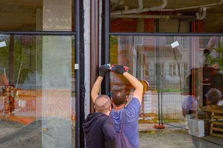 Worker uses ACU power tool, hand drill to screw, twists, tightens screws trough glass holder to...