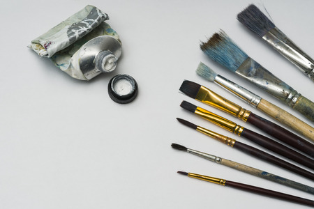 Several brushes of different sizes are on white paper. next to them is a used tube of white paint. Copy space.の写真素材