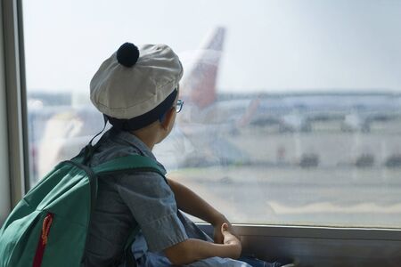 A boy with a backpack in a sailor cap sitting at the window at the airport. Outside the window we could see the silhouette of the aircraft. Copy space.の写真素材