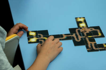 A cut-off image of a child collecting a puzzle picture on the table. The blue background shows the hands of a child and a few connected puzzles. Selective focus.の写真素材