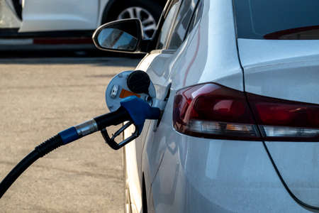 The refueling gun is inserted into the fuel tank of a white car. Left-side view.