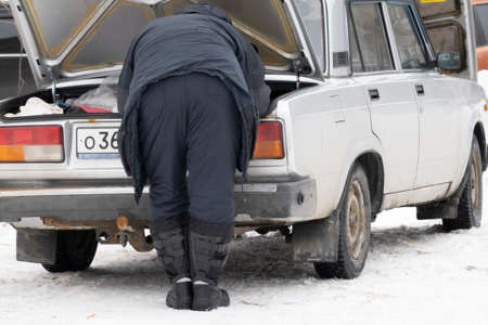 Winter sketch. A man in warm clothes leaned over the open trunk of an old rusty car. He's going...