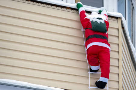 Christmas decor. Figure of decorative Santa Claus on the facade of the house. Santa Claus with a bag of gifts climbs the rope ladder. Copy space.の写真素材