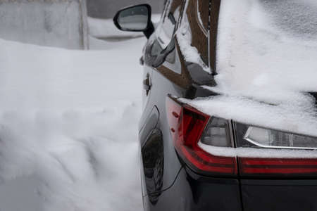 A snow-covered black car stands on the street among snowdrifts. Copy space.の写真素材